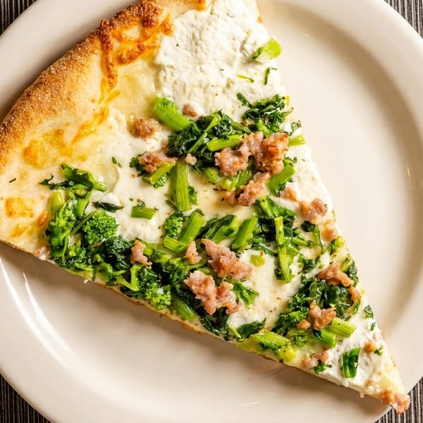 A slice of white pizza with broccoli rabe and sausage on a white plate.