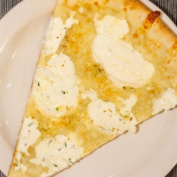 A slice of white pizza with ricotta cheese and herbs on a white plate.