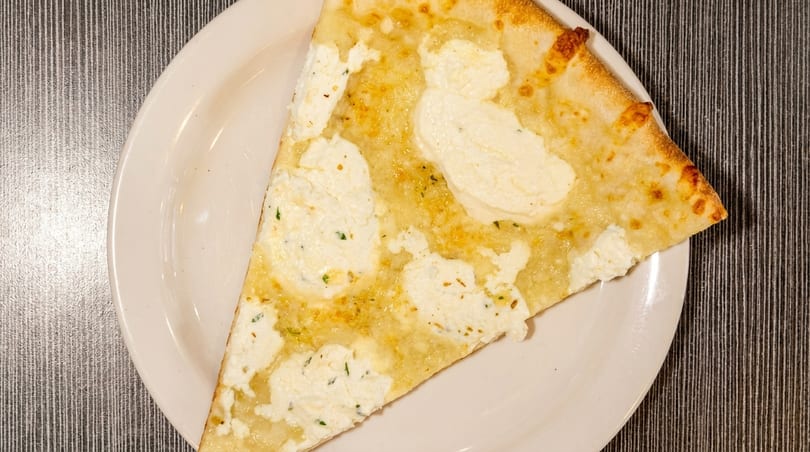 A slice of white pizza with ricotta cheese and herbs on a white plate.